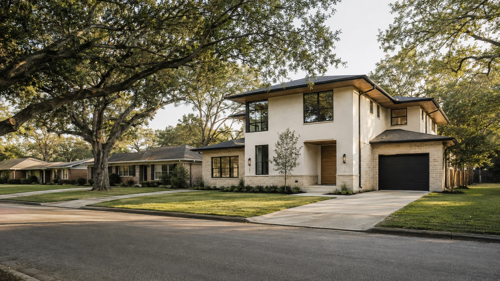 A quiet residential street of single-storey brick and timber houses under mature live oaks in Houston, with a newly built two-storey modern house set among them